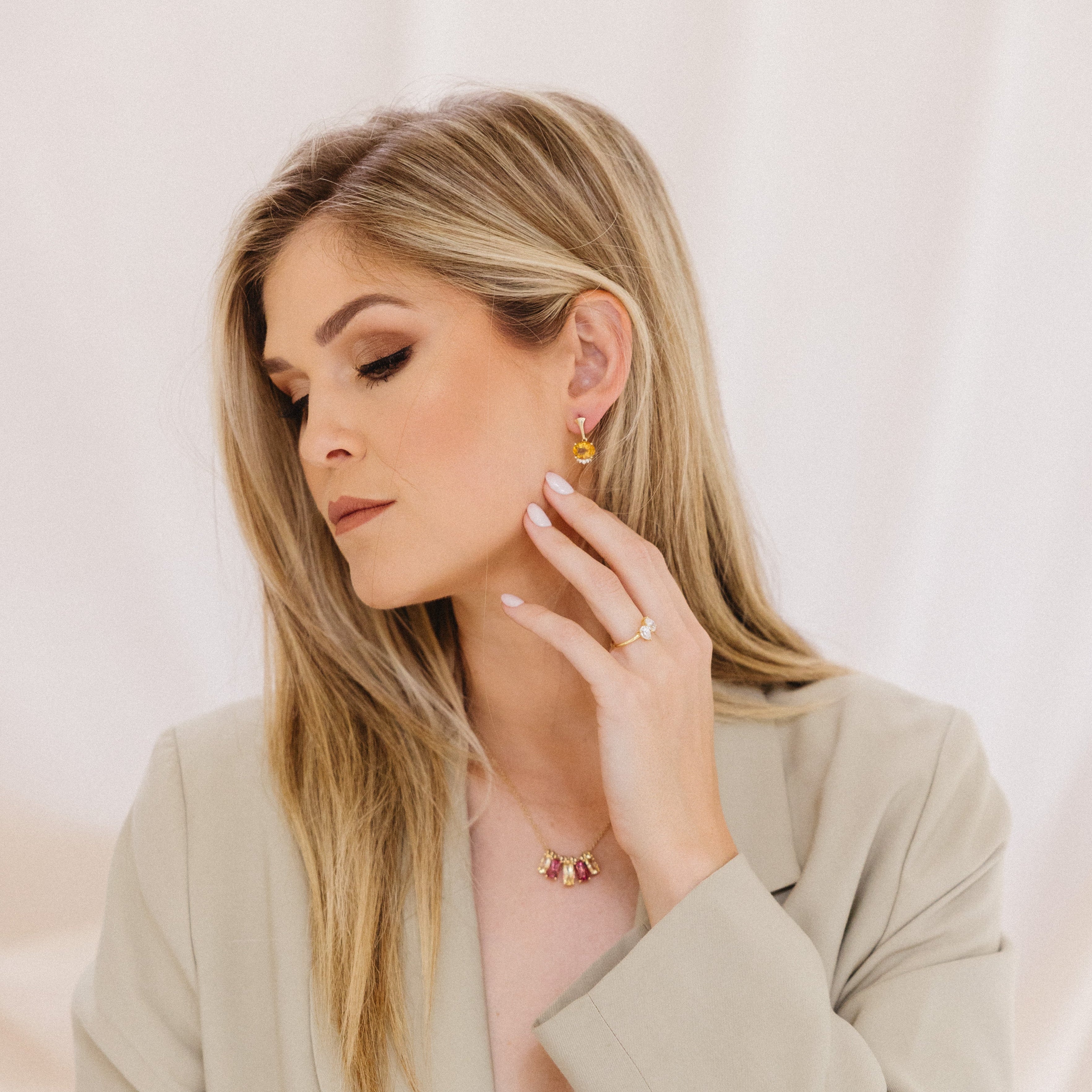 Woman wearing gold jewelry including earrings and a necklace against a light background